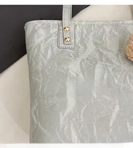 Detail of light gray tote bag featuring wrinkled texture and gold fashion logo engraving