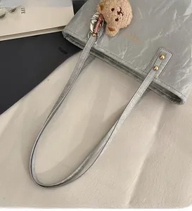 Detail of grey leather tote bag with gold logo, metal rivets and teddy bear charm
