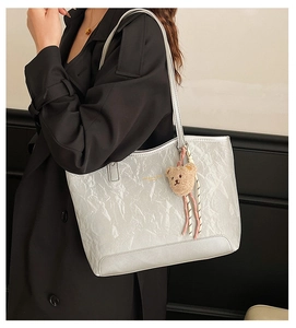 Detail of silver metallic tote bag with wrinkled texture and brown plush bear charm