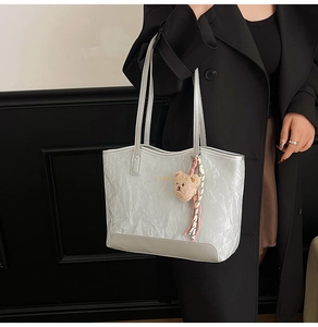 Detail of silver tote bag with crinkled texture, plush bear charm and silk scarf on model