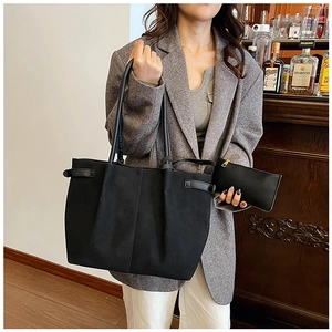 Detail view of a black suede tote bag set with a matching pouch in a casual office setting
