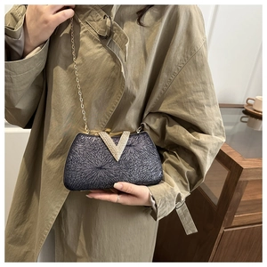 Detail of glittery navy evening clutch bag with gold V-buckle and chain strap on model
