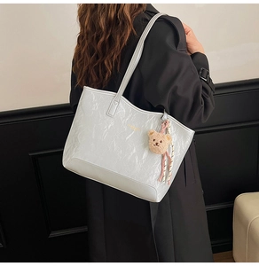 Close-up of silver tote bag with crinkled texture, golden logo, and cute bear charm