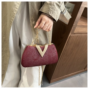 Detail of burgundy evening clutch bag featuring gold V-shaped rhinestone buckle and texture