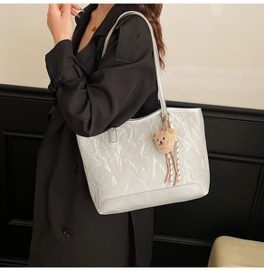 Close-up of metallic silver pleated tote bag with golden print and bear charm on model
