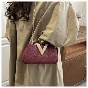 Burgundy clutch bag with gold chain strap and V-shaped rhinestone buckle on a green coat