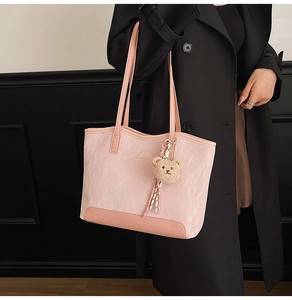 Detail view of pink pleated tote bag with plush bear charm and leather texture