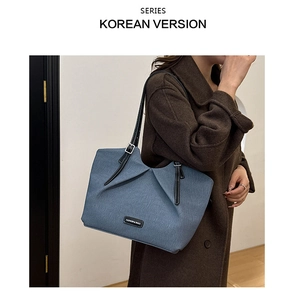Detail of light blue denim tote bag featuring white stitching on black leather straps