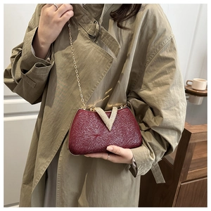 Macro detail of wine red evening clutch with laser texture and V-shaped gold buckle