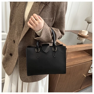 Detail of a black pebbled leather tote bag with light gold hardware and flap closure