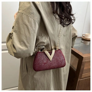 Detail of burgundy evening clutch bag with metallic texture, V-shaped crystal buckle and chain