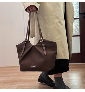 Close-up of pleated dark brown tote bag with metal buckle and logo plaque details