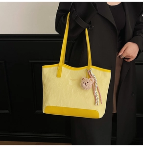 Detail of yellow wrinkled tote bag with bear charm worn with a stylish black coat