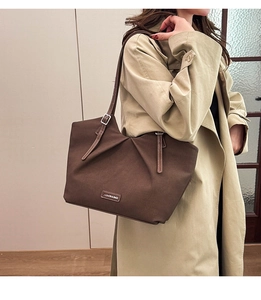 Close-up of pleated detail and brand logo on a brown minimalist tote bag