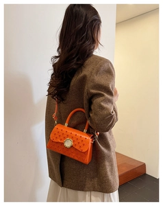 Détail du sac bandoulière orange matelassé avec clous et boucle bijou sur le mannequin
