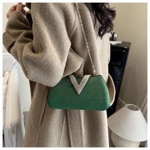 Detail of green evening bag with diamond V-clasp and gold chain on beige coat