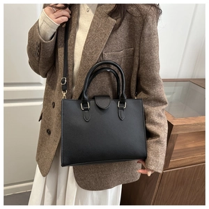 Dettaglio borsa a mano nera in pelle martellata con fibbie dorate su blazer tweed