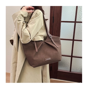 Detail of coffee tote bag with pleated design and metal logo tag worn by a model
