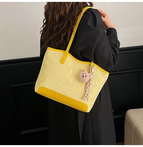 Detail of yellow vintage tote bag featuring a cute plush bear charm and textured material