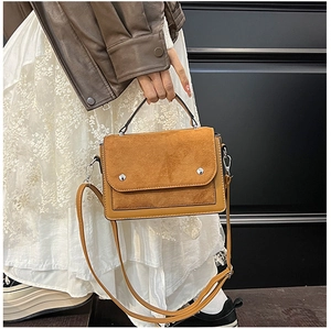 Detail of a brown leather and suede tote bag with metallic silver accents on a white dress