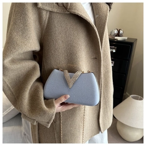 Detail of light blue clutch with gold V-rhinstone and chain on a camel coat