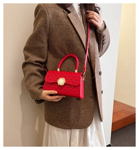 Détail d'un sac bandoulière en cuir rouge avec texture cloutée et fermoir en perle métal