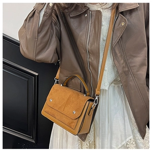 Close-up of retro square bag with suede flap and dual metal buckle detail on model