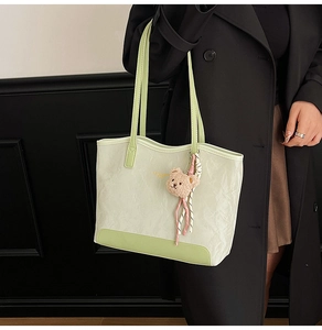 Detail of mint green leather tote with褶皱纹理 and cute plush bear charm decoration