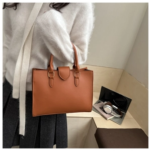 Dettaglio borsa a mano color caramello con finiture dorate in un ambiente ufficio