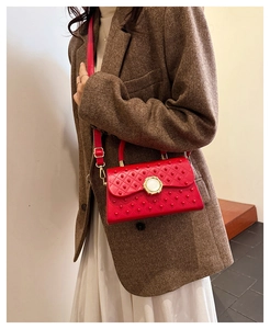 Détail du sac à bandoulière rouge matelassé avec dorures porté sur un blazer brun