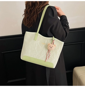 Detail showing the light green and beige contrast tote bag with a pink bear charm