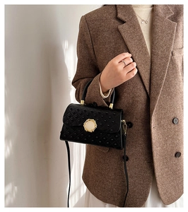 Détail d'un sac noir clouté avec boucle dorée porté sur un blazer en tweed marron