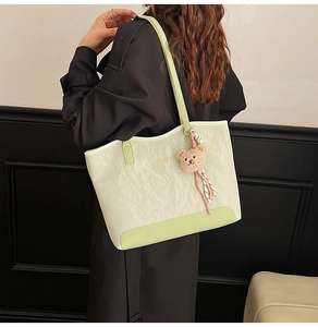 Detailed view of cream and green tote bag with pleated texture and bear charm