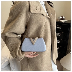 Detail of light blue clutch featuring a gold rhinestone-encrusted V-buckle and chain strap