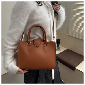 Brown lychee leather tote bag with gold hardware shown on model in soft natural light
