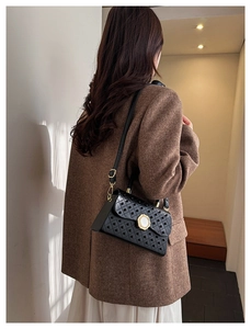 Détail du sac bandoulière noir avec rivets métalliques et boucle blanche sur l'épaule