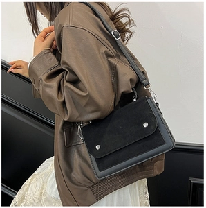 Detail of black square crossbody bag showing leather texture and silver rivets on the flap