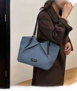 Detail of blue denim tote bag featuring adjustable black leather straps and fashion label