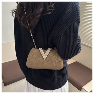 Detail of gold evening clutch bag with starburst texture and rhinestone V buckle on model