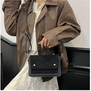 Detail of black leather crossbody bag with silver buckle and removable strap shown on model