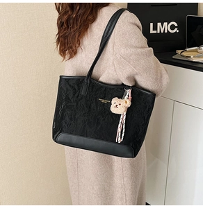 Detail of black pleated tote bag featuring a gold fashion logo and plush bear charm