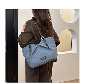 Detail of blue denim tote bag with black leather handles and fashion logo plaque