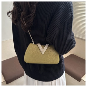 Detail of gold glitter clutch bag with crystal V-buckle and fine chain strap on model
