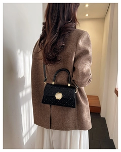 Détail du sac matelassé noir avec clous dorés porté par un mannequin en intérieur