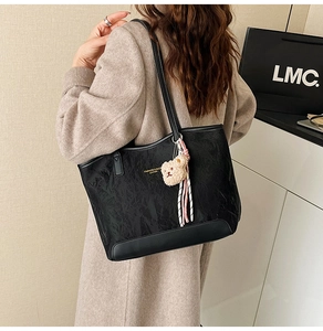 Detail of black wrinkled tote bag with golden lettering and cute bear charm accessory