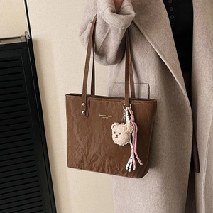 Brown vintage leather tote bag with plush bear charm shown on model in urban style