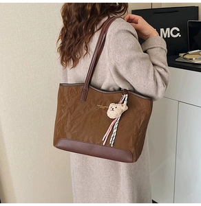Detail of brown pleated leather tote bag with teddy bear charm and striped ribbon accent