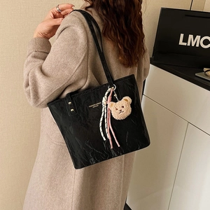 Fashionable black glossy tote bag with crinkle texture and cute bear charm worn by a model