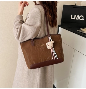 Detail of brown tote bag with wrinkled texture, leather trim and plush bear charm