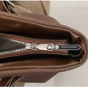 Close-up of smooth silver metal zipper and white contrast stitching on brown leather tote